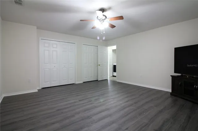 a view of an empty room with wooden floor and a ceiling fan
