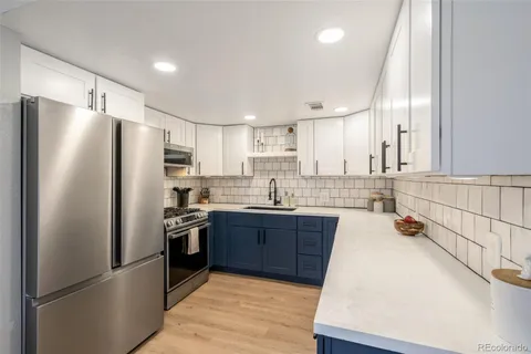 a kitchen with stainless steel appliances granite countertop a refrigerator a sink dishwasher a stove and white cabinets with wooden floor