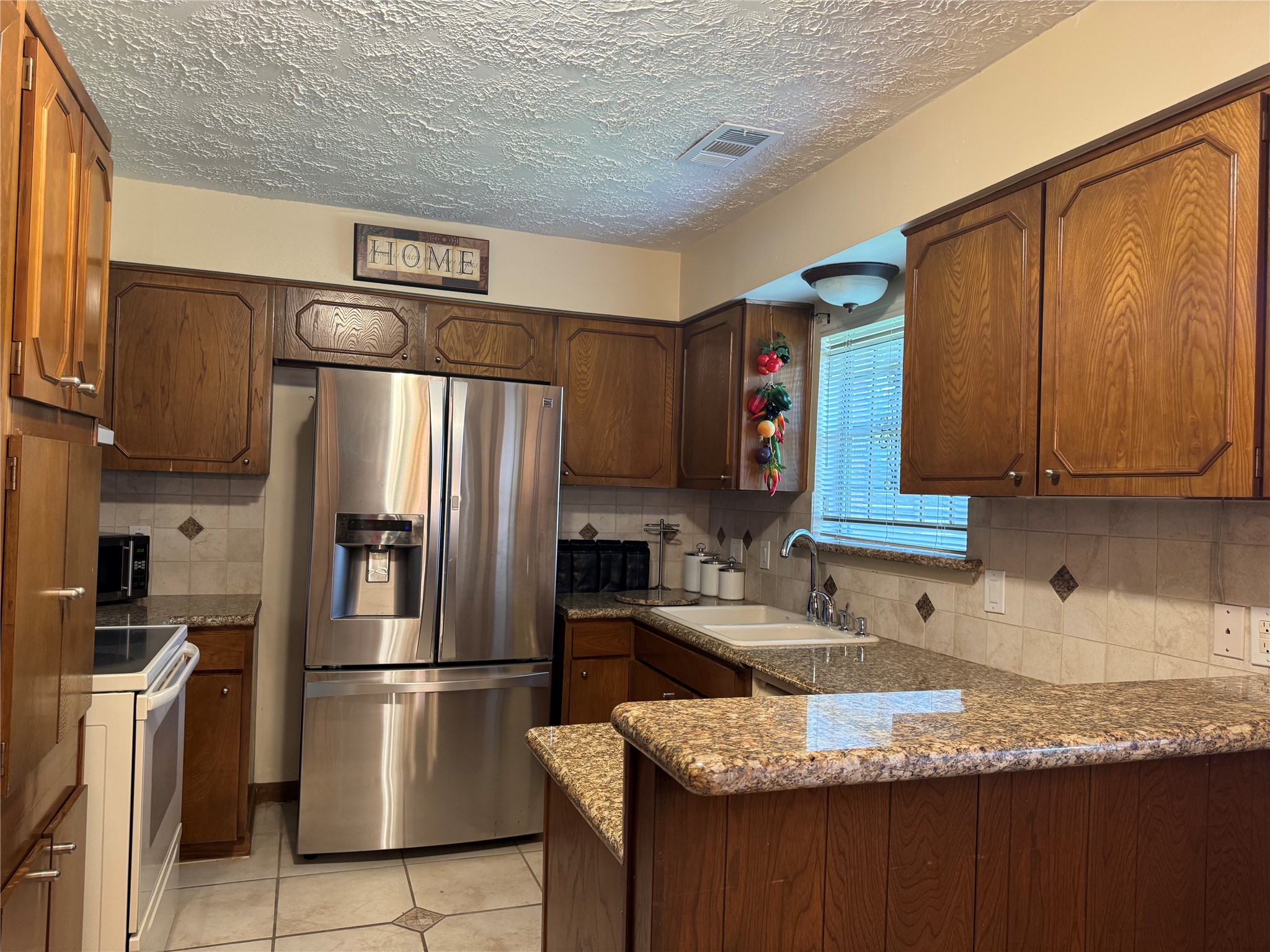 203 East Thornton Road Houston, TX 77022 - Photo 7 of 18 Kitchen features warm wooden cabinetry with a spacious granite countertop. The tile backsplash and window provide a cozy yet functional space.