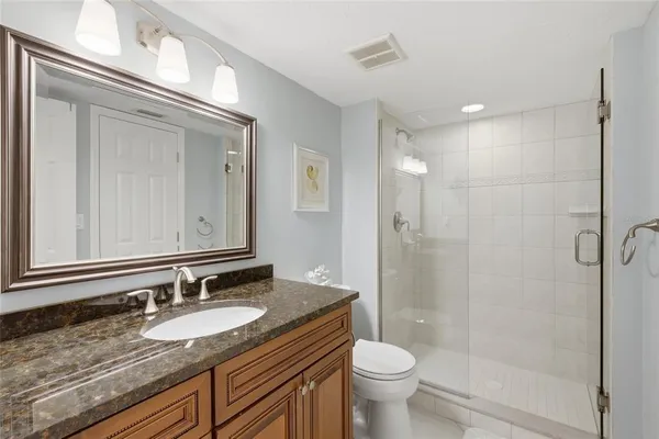 a bathroom with a granite countertop sink a toilet a mirror and shower