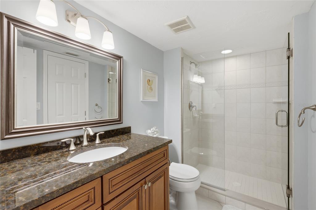 1750 Benjamin Franklin Drive, Unit 9B Sarasota, FL 34236 - Photo 26 of 47 a bathroom with a granite countertop sink a toilet a mirror and shower