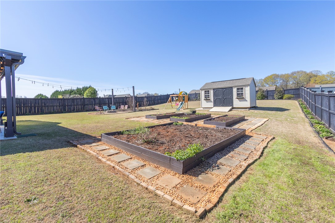 203 Graceview West Anderson, SC 29625 - Photo 39 of 50 The expansive yard features garden beds, a storage shed, and a play area, all enclosed by fencing.