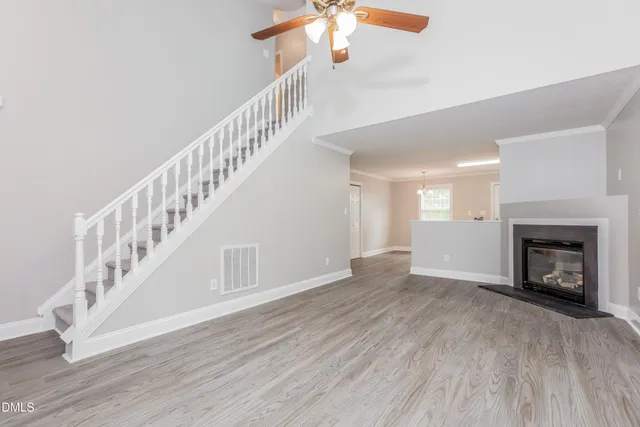 a view of an empty room with wooden floor a chandelier and a fireplace