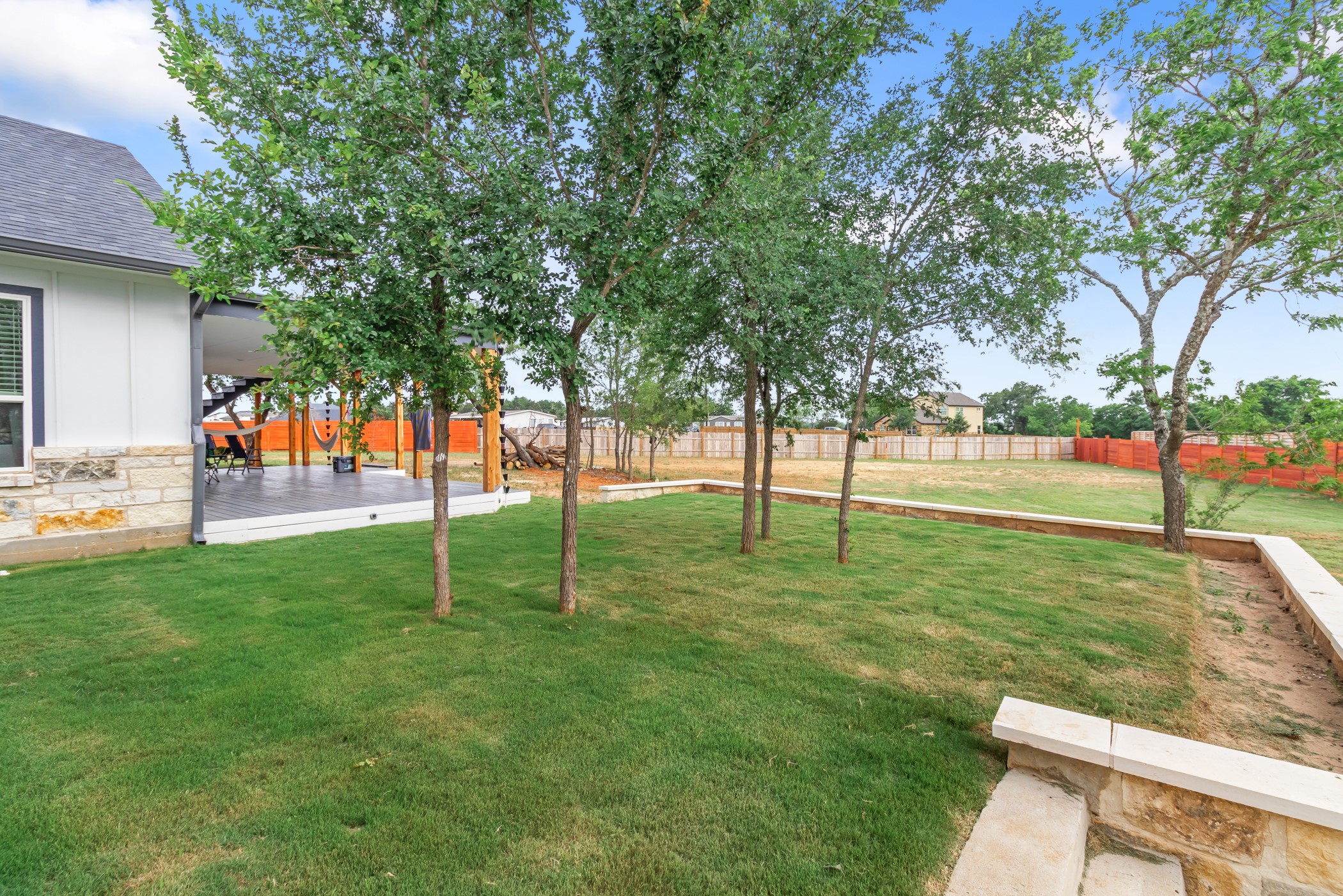 123 Zacate Street Elgin, TX 78621 - Photo 32 of 33 Expansive backyard featuring a covered patio, stone retaining walls, mature trees, and a spacious lawn area