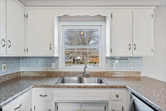 a kitchen with granite countertop a sink a window and cabinets