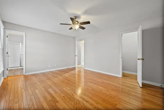 an empty room with wooden floor fan and windows