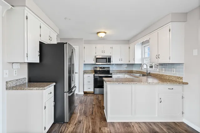 a kitchen with granite countertop a refrigerator stove and sink with wooden floor