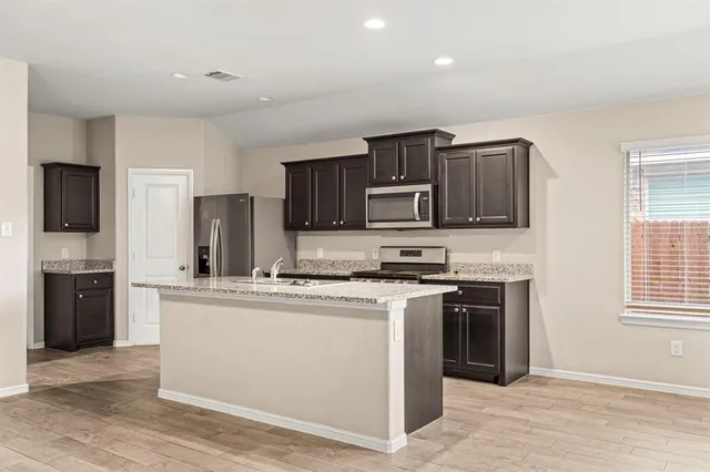 a kitchen with stainless steel appliances granite countertop a stove top oven a sink dishwasher a refrigerator and a microwave oven with wooden floor