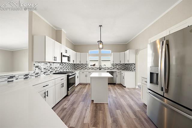 8160 Edison Road Yoder, CO 80864 - Photo 19 of 42 Kitchen with a kitchen island, white cabinets, appliances with stainless steel finishes, backsplash, and light wood-type flooring