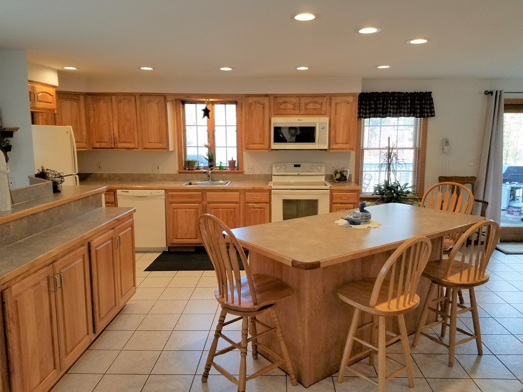 52 School House Road Groton, MA 01450 - Photo 23 of 27 a kitchen with stainless steel appliances granite countertop a stove a sink a microwave a island with a dining table and chairs