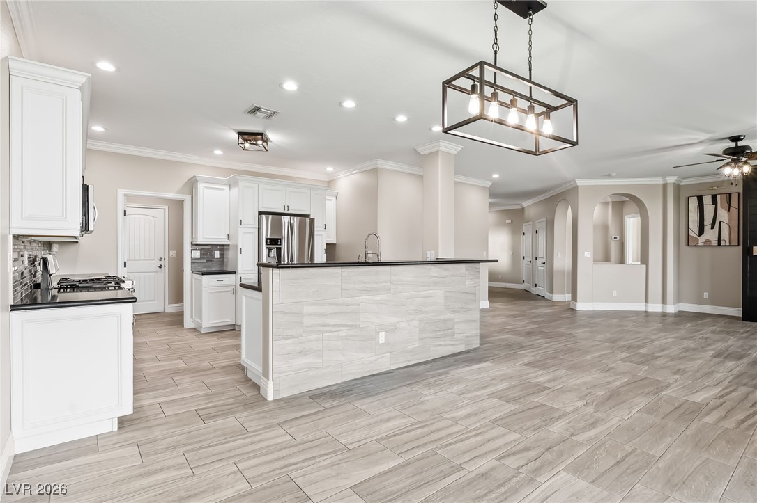 3807 Chapels Royal Street Laughlin, NV 89029 - Photo 17 of 62 Kitchen featuring crown molding, a center island with sink, white cabinets, hanging light fixtures, and stainless steel appliances