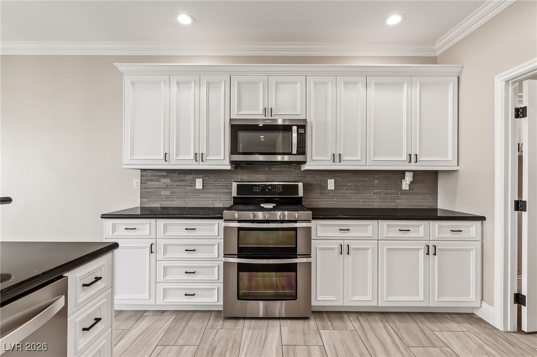 3807 Chapels Royal Street Laughlin, NV 89029 - Photo 19 of 62 Kitchen featuring appliances with stainless steel finishes, white cabinetry, decorative backsplash, recessed lighting, and ornamental molding