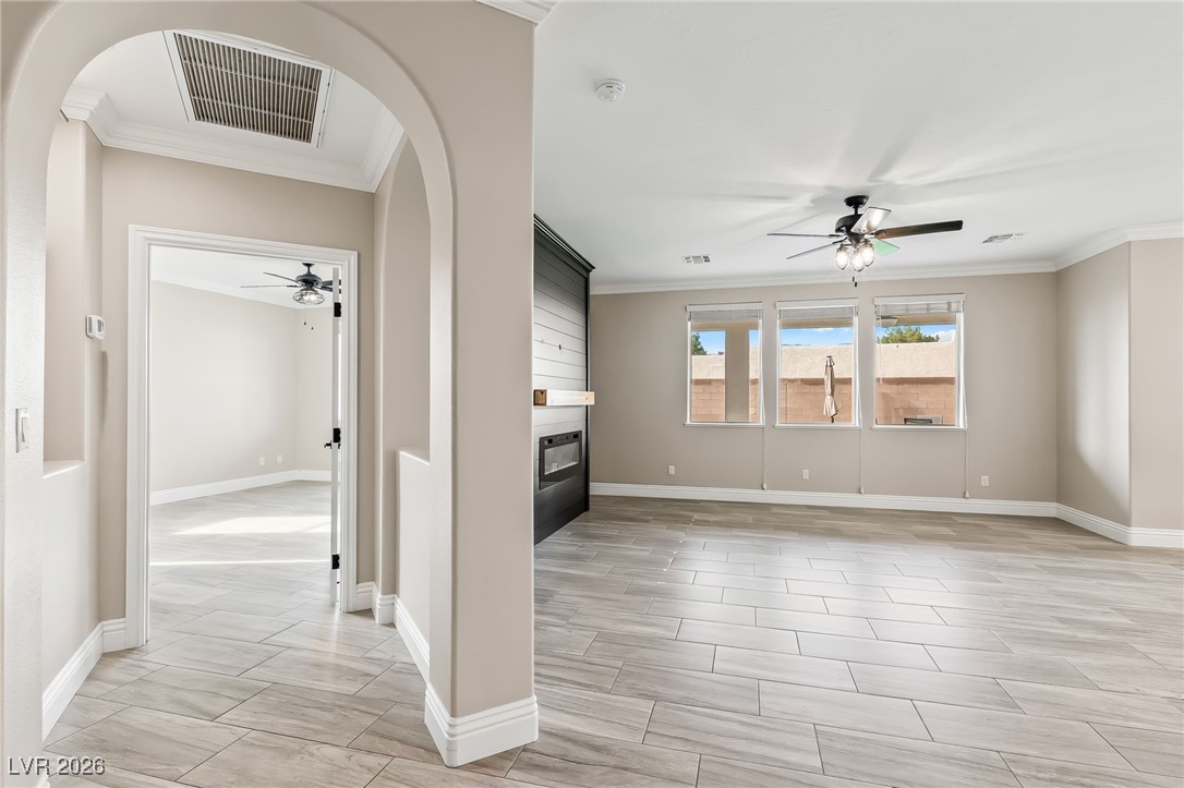 3807 Chapels Royal Street Laughlin, NV 89029 - Photo 6 of 62 Unfurnished living room with a ceiling fan, arched walkways, a fireplace, and ornamental molding