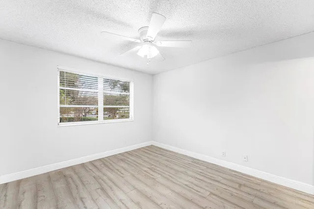 an empty room with wooden floor fan and windows