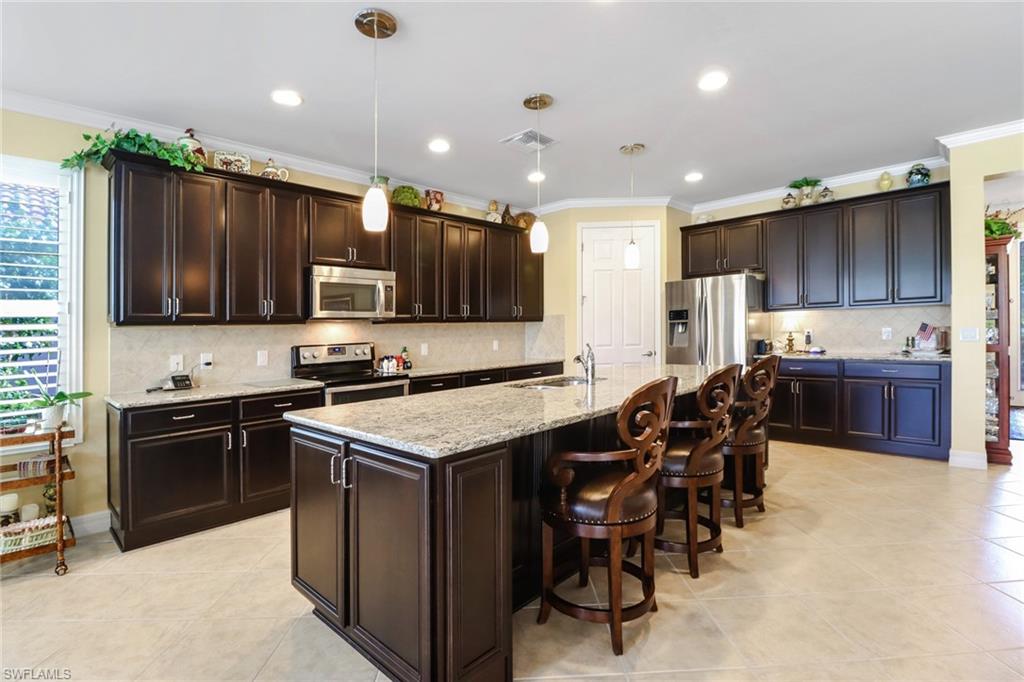 8633 Julia Lane Naples, FL 34114 - Photo 3 of 26 a kitchen with kitchen island granite countertop wooden cabinets and stainless steel appliances
