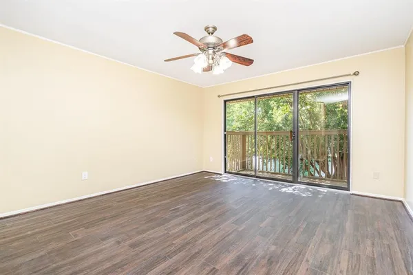 an empty room with wooden floor ceiling fan and windows