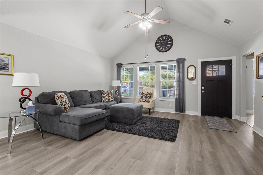 608 East Shepherd Street Denison, TX 75021 - Photo 9 of 31 Living area featuring a vaulted ceiling with a ceiling fan, light wood-finish flooring, a black front door with upper window panes, and three large windows with white blinds