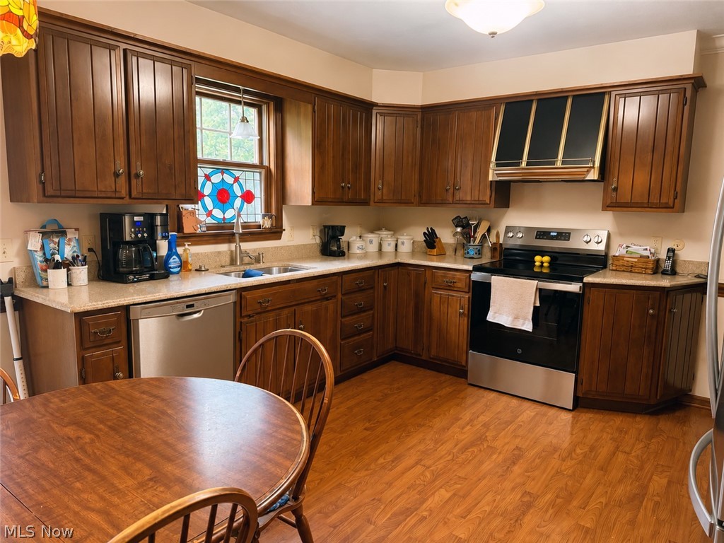 6155 Gibson Road Canfield, OH 44406 - Photo 18 of 43 Expansive kitchen featuring a full suite of stainless steel appliances, abundant wood cabinetry, an integrated sink with a window, light-toned countertops, and wood-finish flooring