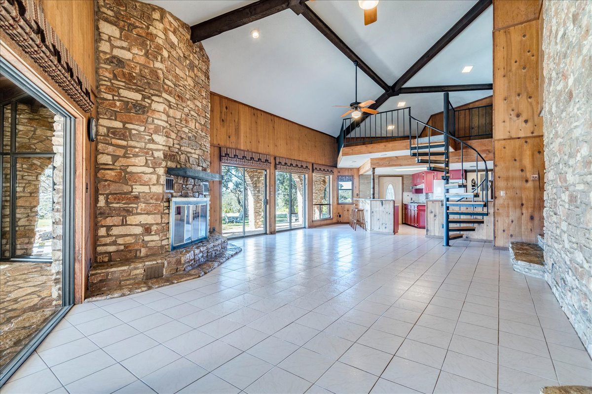 9763 Ranch Road 1623 Blanco, TX 78606 - Photo 12 of 40 Spacious interior featuring a vaulted ceiling with exposed beams, stone-clad fireplace, and expansive tile flooring