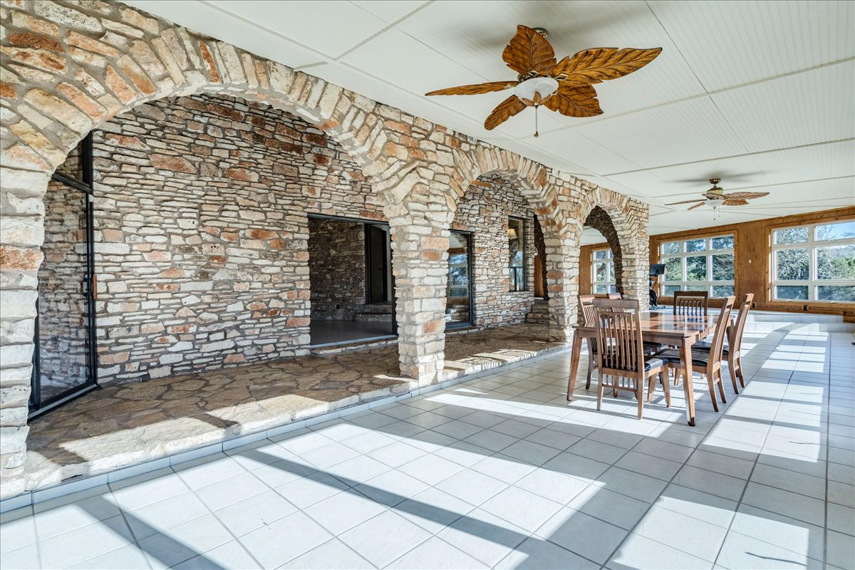 9763 Ranch Road 1623 Blanco, TX 78606 - Photo 15 of 40 Spacious sunroom featuring stone archways and wall accents, white square tile flooring, multiple windows providing abundant natural light, and two decorative ceiling fans