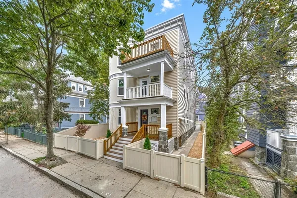 a view of a white house with large trees and couches