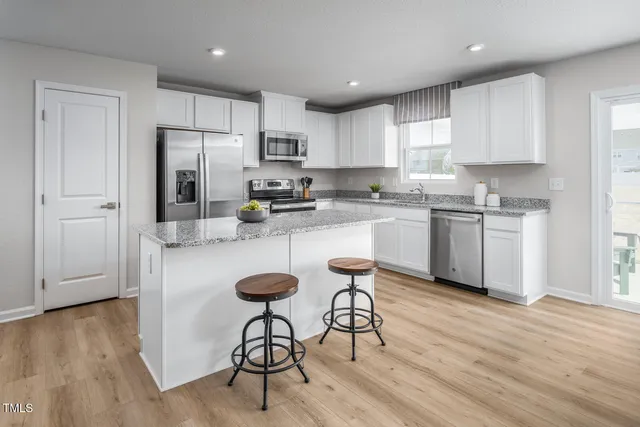 a kitchen with stainless steel appliances granite countertop a stove top oven a refrigerator a sink and white cabinets with wooden floor