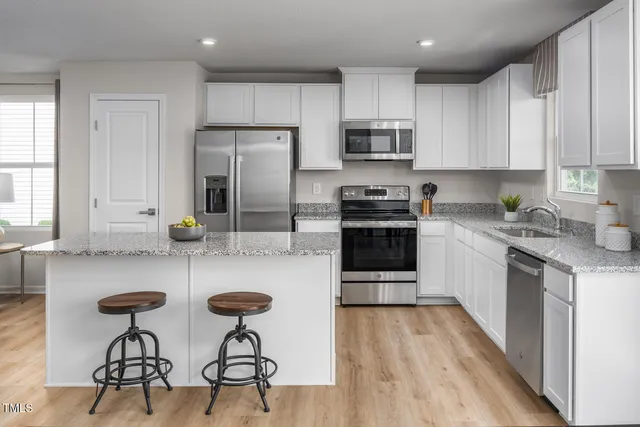 a kitchen with stainless steel appliances granite countertop a stove a sink a refrigerator and white cabinets with wooden floor