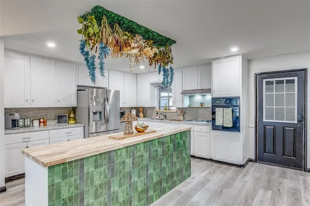 a kitchen with stainless steel appliances granite countertop a refrigerator a sink dishwasher a stove and a dining table with wooden floor