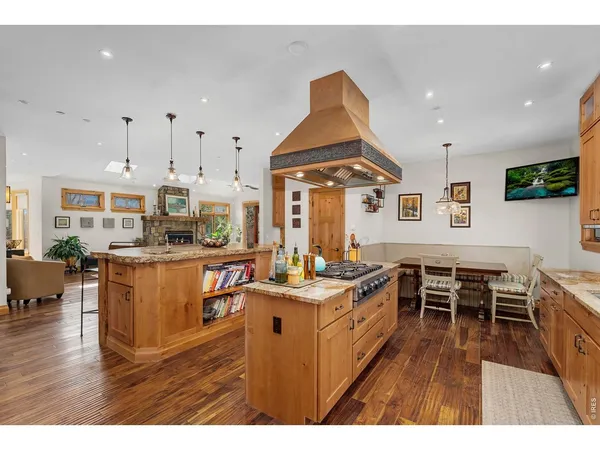 a kitchen with stainless steel appliances granite countertop a stove top oven a sink a dining table and chairs with wooden floor