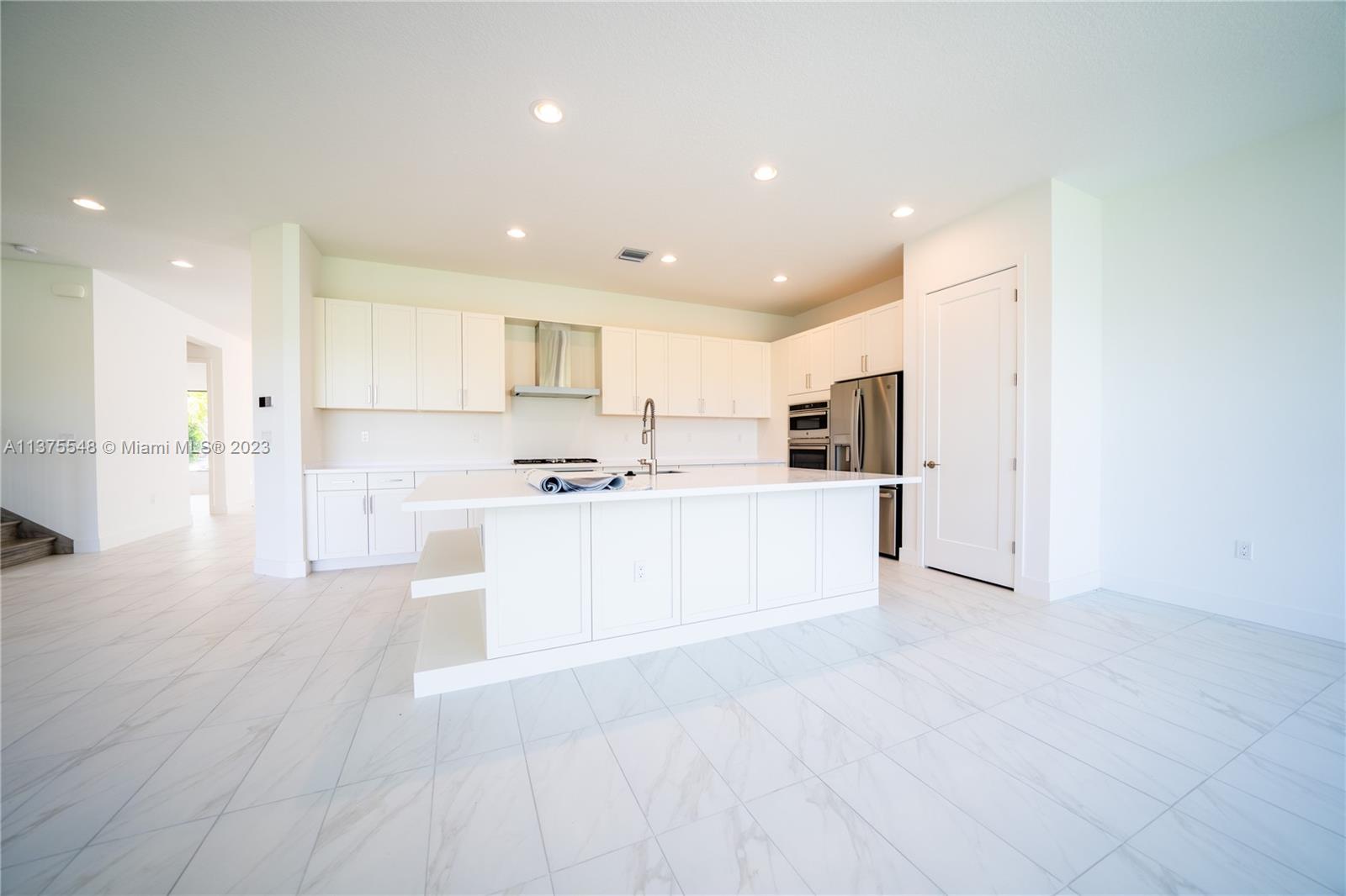 17232 Teton River Road Boca Raton, FL 33496 - Photo 8 of 28 a large kitchen with kitchen island a sink a refrigerator and white cabinets