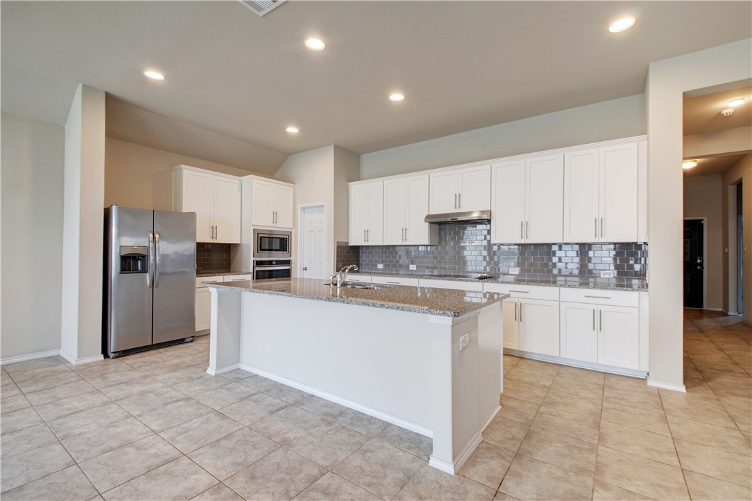 104 Finley Street Hutto, TX 78634 - Photo 11 of 37 a kitchen with granite countertop a refrigerator and white cabinets