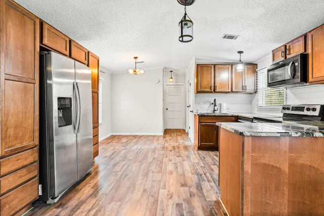 a kitchen with stainless steel appliances granite countertop a refrigerator a stove top oven a sink dishwasher and wooden floor