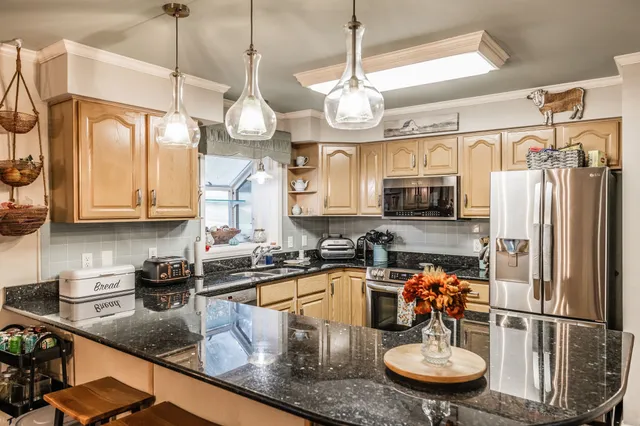 a kitchen with stainless steel appliances granite countertop a sink a refrigerator a stove a dining table and chairs with wooden floor