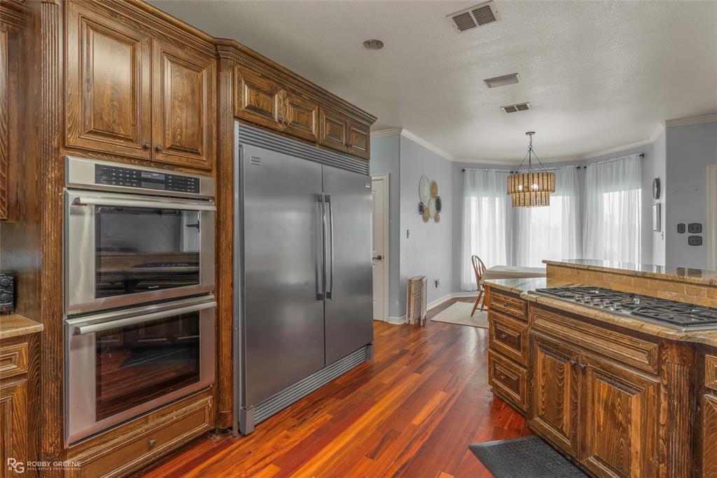 624 Holly Street Grand Cane, LA 71032 - Photo 8 of 40 Kitchen with stainless steel appliances, ornamental molding, wood finish cabinetry, light stone counters, and dark wood-type flooring