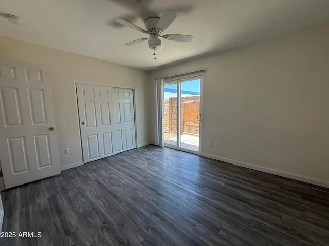 a view of an empty room with wooden floor and a ceiling fan