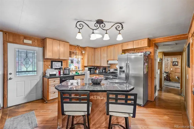 a kitchen with stainless steel appliances granite countertop a refrigerator a stove a sink a dining table and chairs with wooden floor