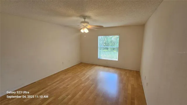 an empty room with wooden floor chandelier fan and windows