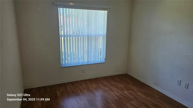 a view of an empty room with wooden floor and a window