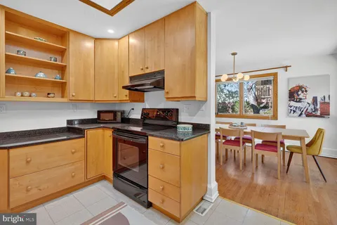 a kitchen with stainless steel appliances granite countertop a stove top oven a sink a dining table and chairs with wooden floor