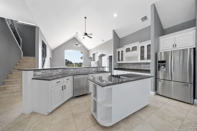 a large kitchen with stainless steel appliances kitchen island granite countertop a stove a sink a refrigerator and white cabinets