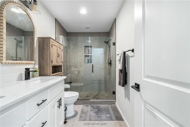 a bathroom with a sink a toilet a glass door shower and a mirror