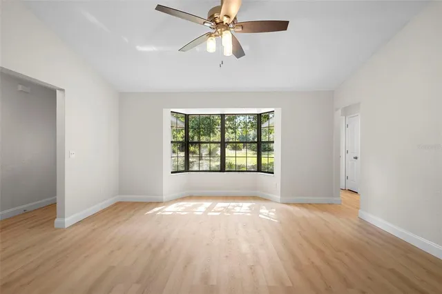 an empty room with wooden floor chandelier fan and windows
