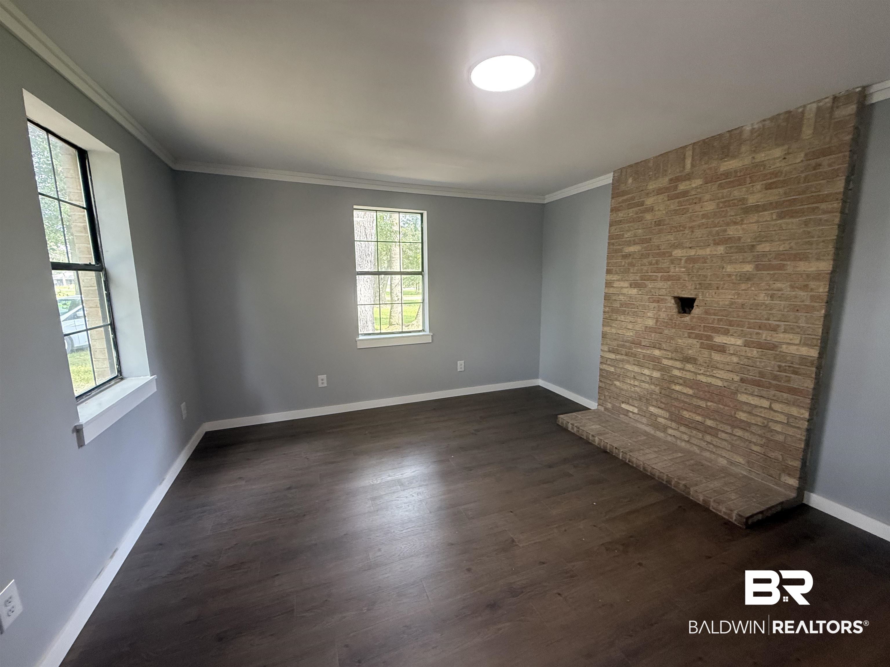 17440 Old Brady Road Bay Minette, AL 36507 - Photo 6 of 9 Empty room featuring dark wood floors, crown molding, and a brick accent wall, offering the versatility to serve as a living area or whatever fits your needs.