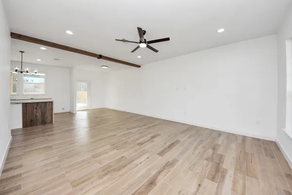 an empty room with wooden floor a ceiling fan and kitchen view