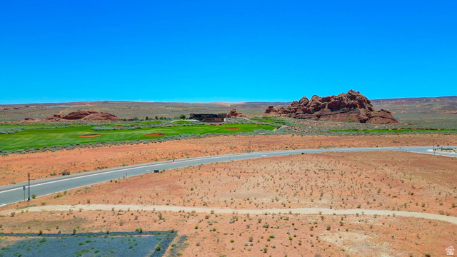 3306 South Endless Trail, Unit 33 Hurricane, UT 84737 - Photo 23 of 27 Expansive desert lot featuring a paved road, scattered vegetation, and distant green golf course elements