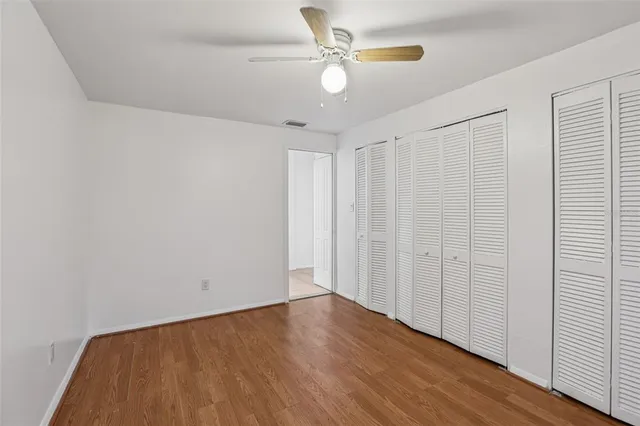 an empty room with wooden floor fan and windows