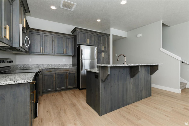 226 South 600 West Logan, UT 84321 - Photo 7 of 25 Kitchen featuring stainless steel appliances, a center island with sink, light wood-type flooring, light stone counters, and a textured ceiling