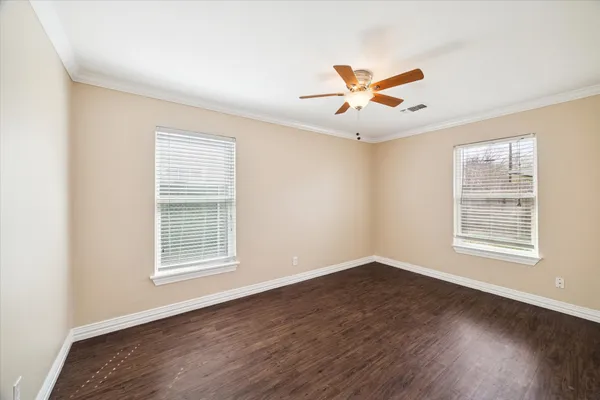an empty room with wooden floor ceiling fan and windows