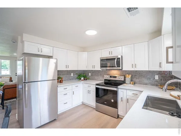a kitchen with stainless steel appliances granite countertop a refrigerator stove a sink and white cabinets