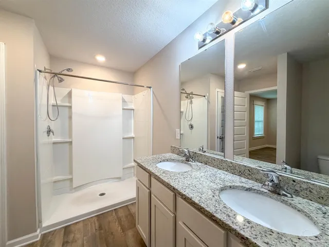 a bathroom with a granite countertop double vanity sink and shower